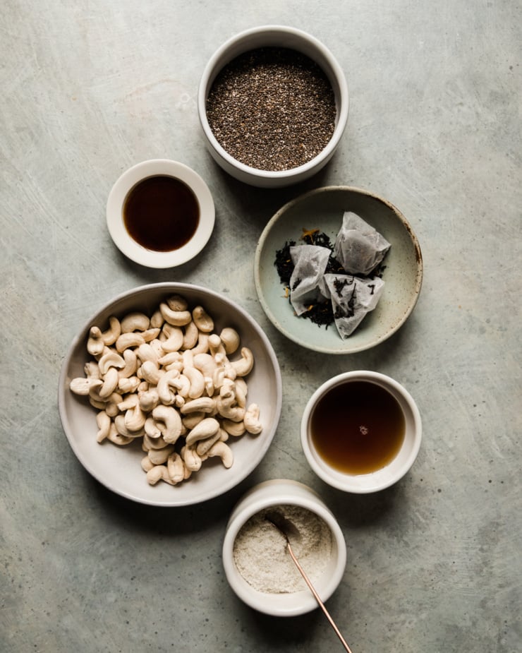 An overhead shot shows all ingredients needed for an earl grey latte chia pudding recipe: raw soaked cashews, chia seeds, vanilla bean paste, maple syrup, salt, and earl grey tea.