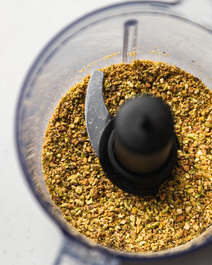 An up close, overhead shot shows finely ground pistachios in the bowl of a mini food processor.