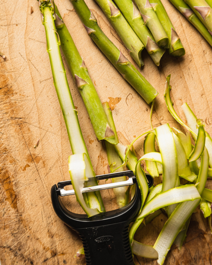 An up close, overhead shot shows a Y peeler making thin "ribbons" out of asparagus spears.