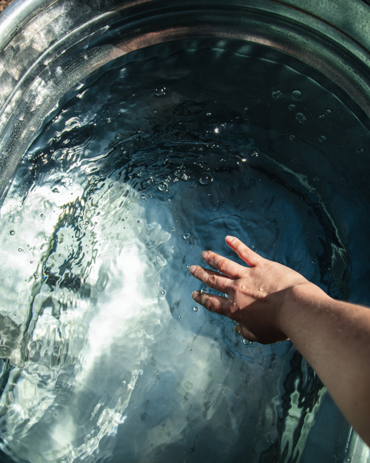 An overhead image shows a hand splashing up some water in a galvanized metal stock tank that is full of water.
