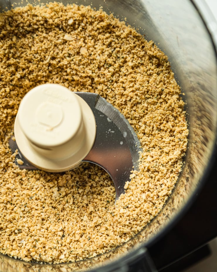 An overhead shot shows vegan "parmesan" freshly mixed in the bowl of a food processor. The texture is like a fine meal consistency.