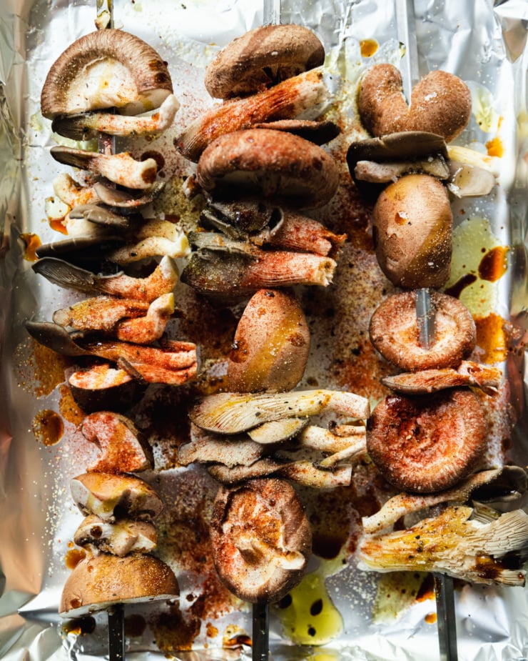 An overhead shot shows skewers of mushrooms that have been drizzled with oil and dusted with spices.
