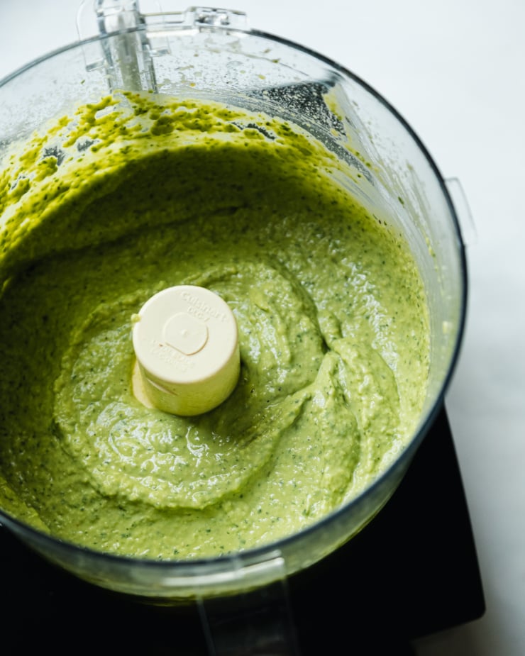 A 3/4 angle shot shows herby whipped white beans in the bowl of a food processor.