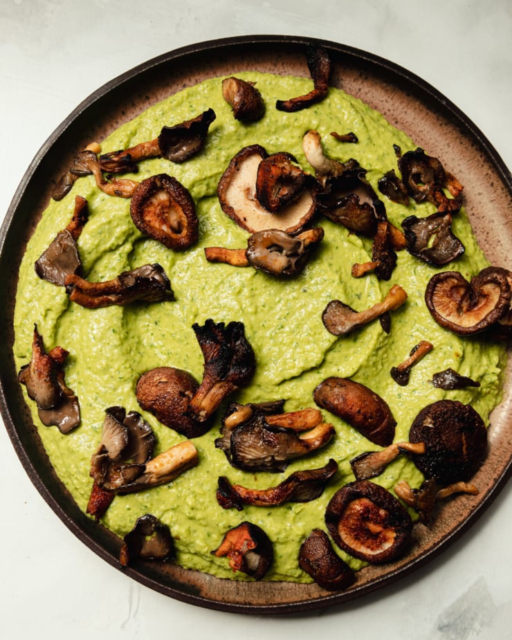 An up close, overhead shot shows a platter of herby whipped white beans that are topped with smoky grilled mushrooms.
