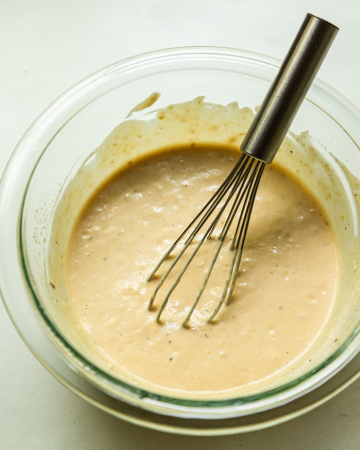 An overhead shot shows a small bowl filled with a creamy hummus-based dressing. A small whisk is sticking out of the bowl.