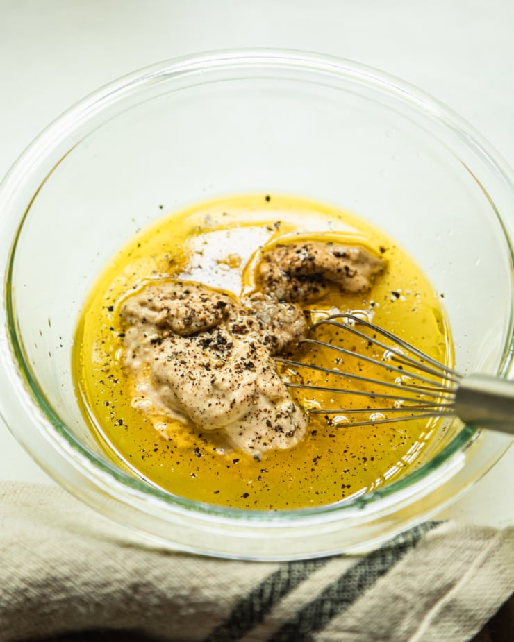 A 3/4 angle shot shows a small bowl with hummus, lemon juice, water, olive oil, salt, pepper, and dijon mustard.