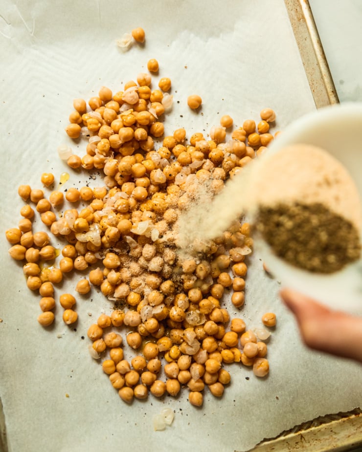 An overhead shot shows spic es being poured onto chickpeas.