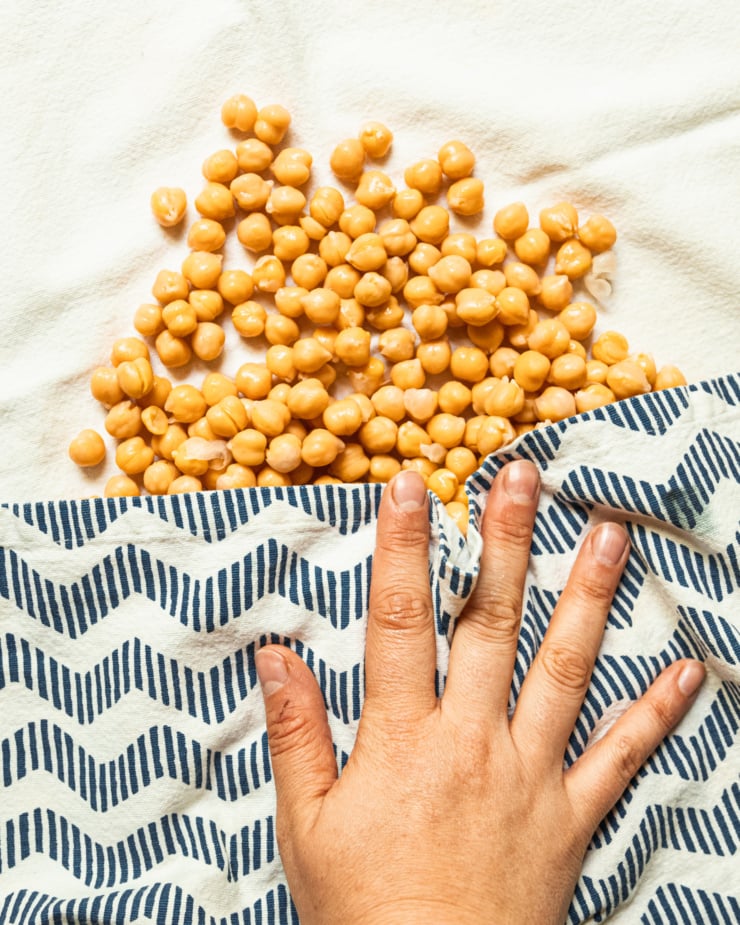 An overhead shot shows a hand blotting chickpeas dry with a dish towel.