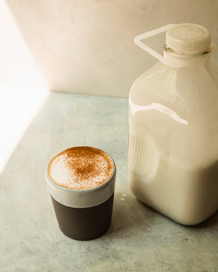 A 3/4 angle shot shows a bottle of nut milk and a latte topped with cinnamon nearby