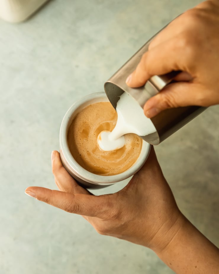 An overhead shots a hand pouring frothy milk into a cup of espresso.