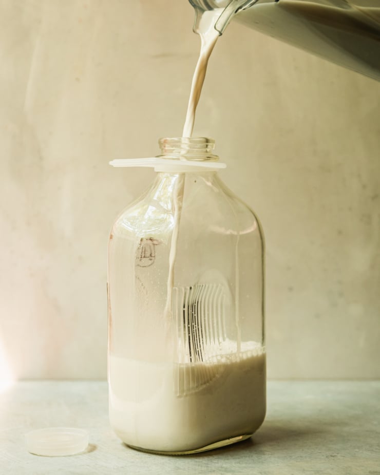 A head-on shot shows a glass jug being filled with nut milk.