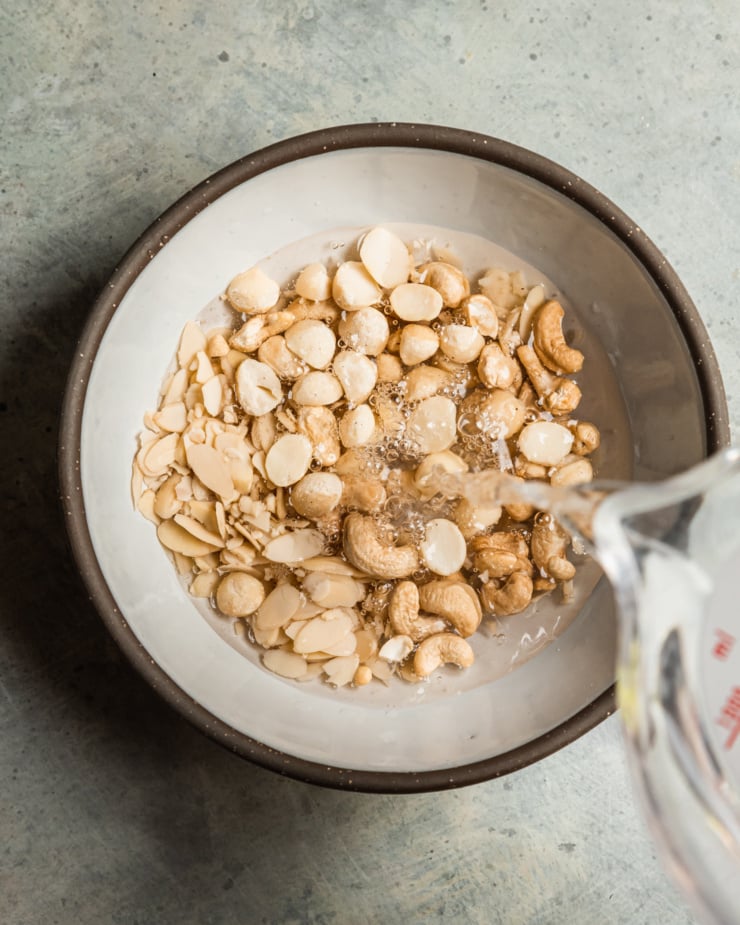 An overhead shot shows a trio of nuts in a bowl with water being poured over top.