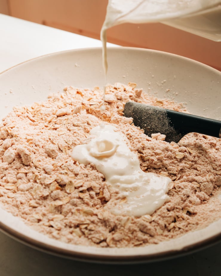 A 3/4 angle shot shows a vegan "buttermilk" being poured into a bowl with a flour, oat, and vegan butter mixture.