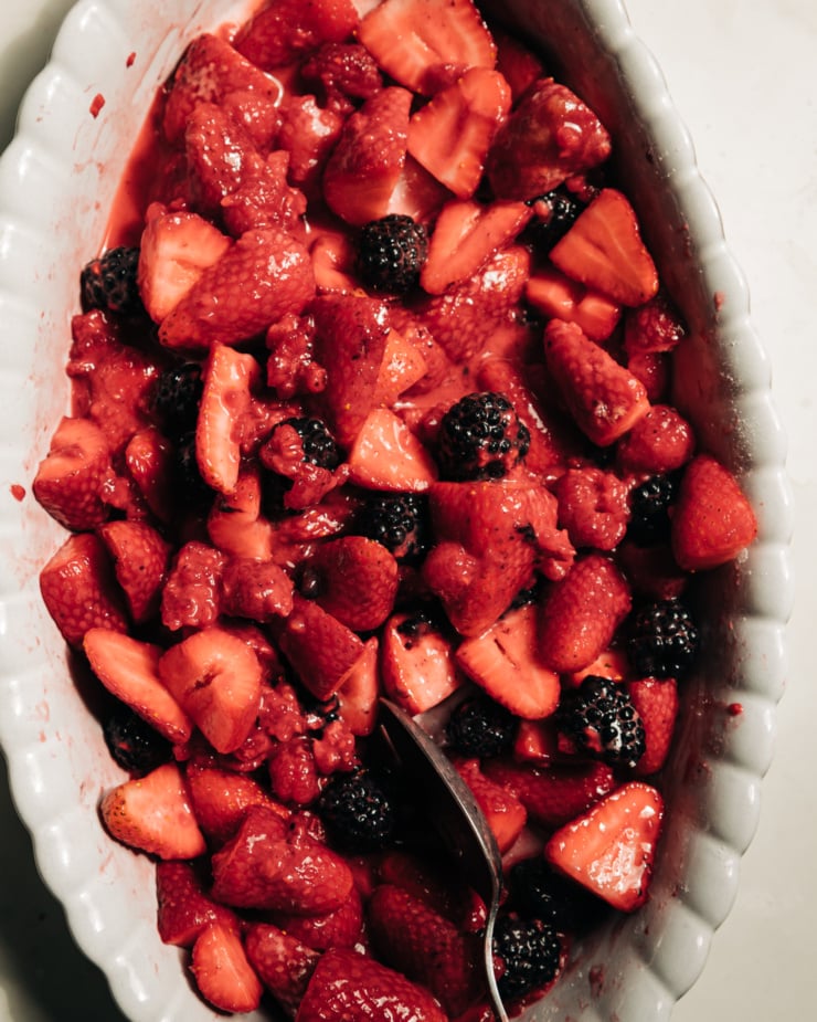 An overhead shows macerated mixed berries in an oval-shaped baking dish.