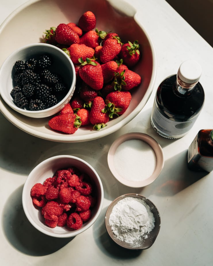 An overhead shot shows raspberries, blackberries, strawberries, sugar, wild berry balsamic vinegar, arrowroot starch, and vanilla extract.