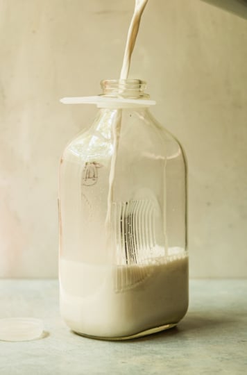A head-on shot shows a glass jug being filled with nut milk.