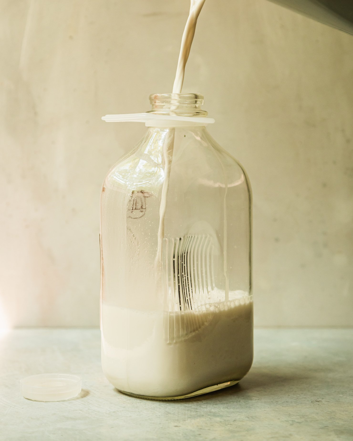 A head-on shot shows a glass jug being filled with nut milk.