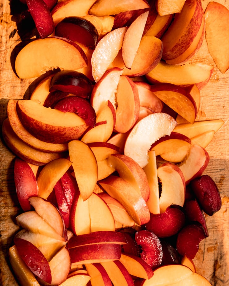 An overhead shot shows a bunch of sliced stone fruit on a worn wooden cutting board.
