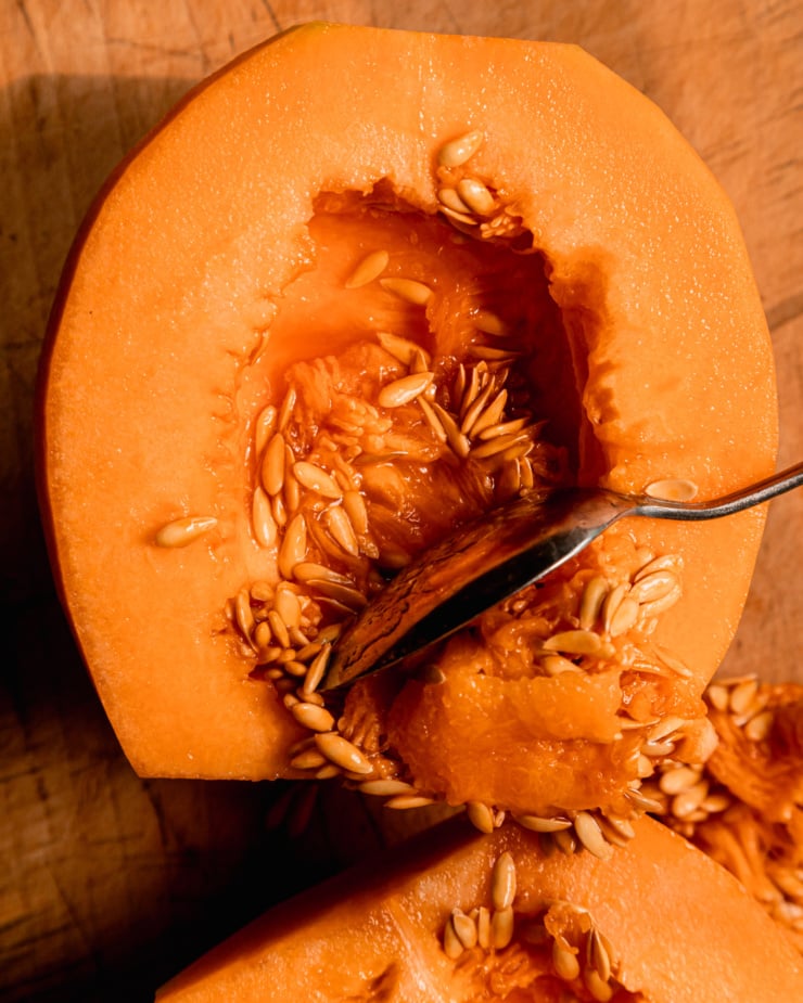 An up close, overhead shot shows the seeds being scooped out of a halved cantaloupe.