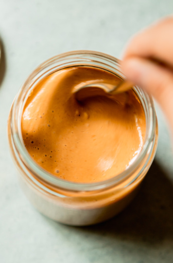 An overhead shot shows a hand using a spoon to stir up a jar of peanut sauce.