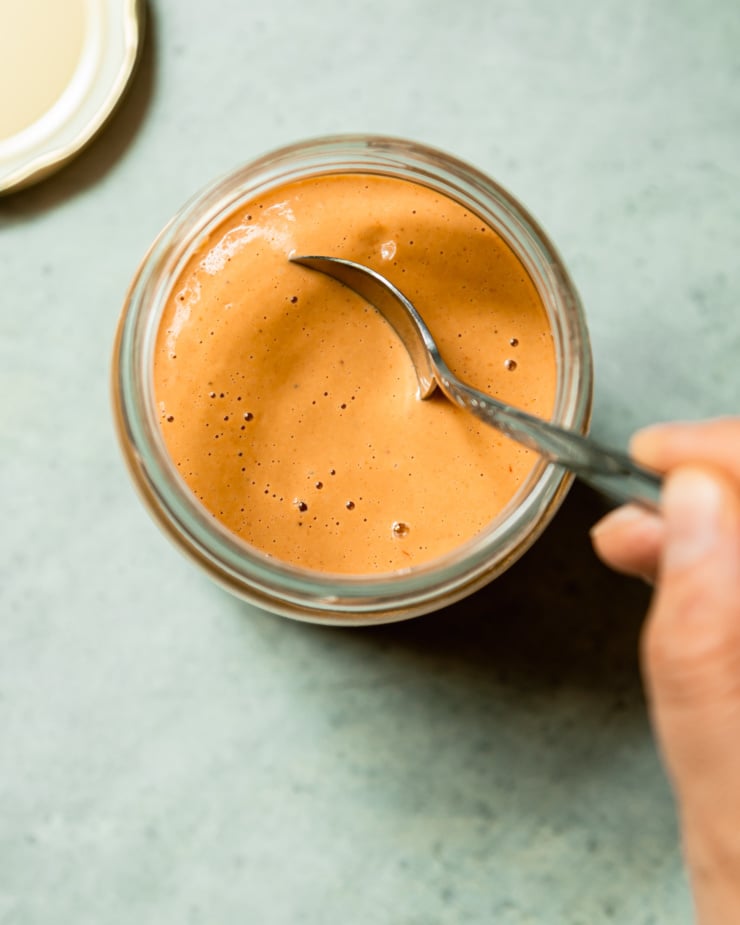 An overhead shot shows a hand dipping a spoon into a jar of peanut sauce.
