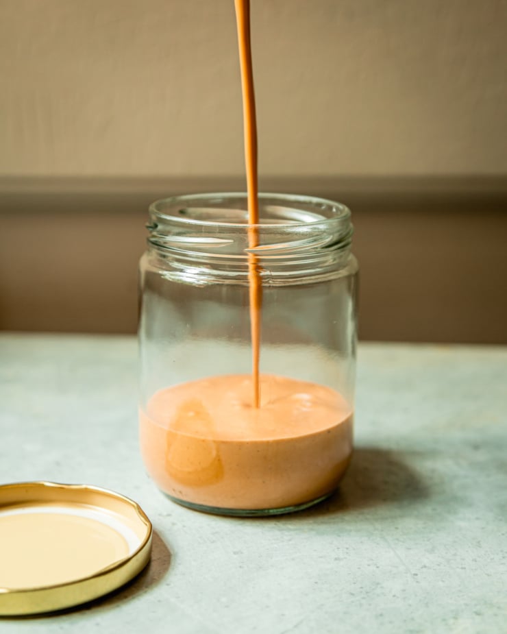 A head-on shows peanut sauce being poured into a glass jar.