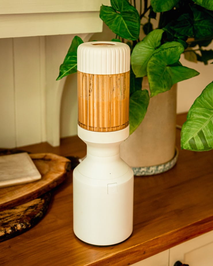 A slight 3/4 angle image shows a sauce being blended up in a personal blender on a wood countertop.