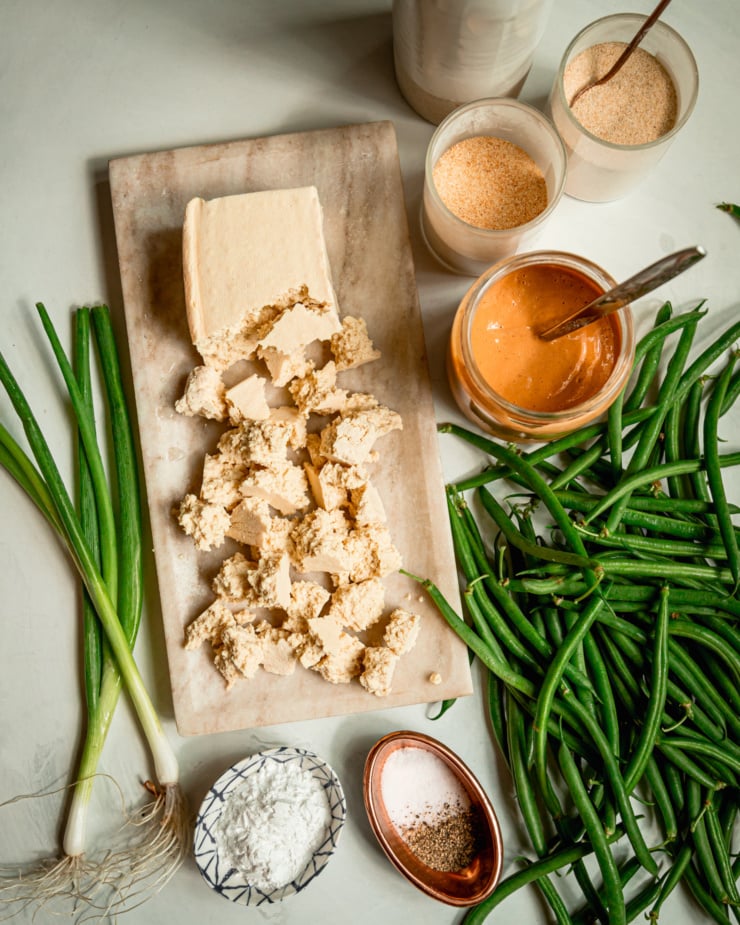 An overhead shot of ingredients for a tofu and green bean dinner with spices, a sauce, and green onions.