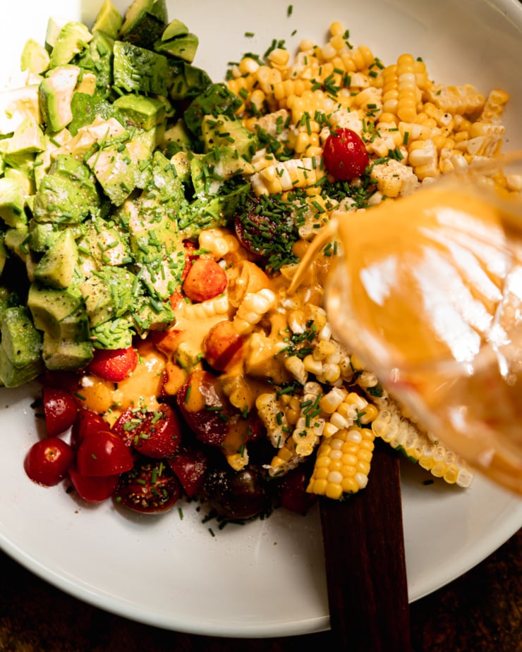 An overhead shot shows a slightly creamy dressing being poured over a chopped salad with corn.