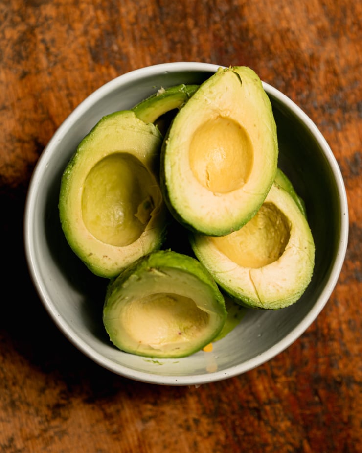 An overhead shot shows peeled avocado halves in a bowl.