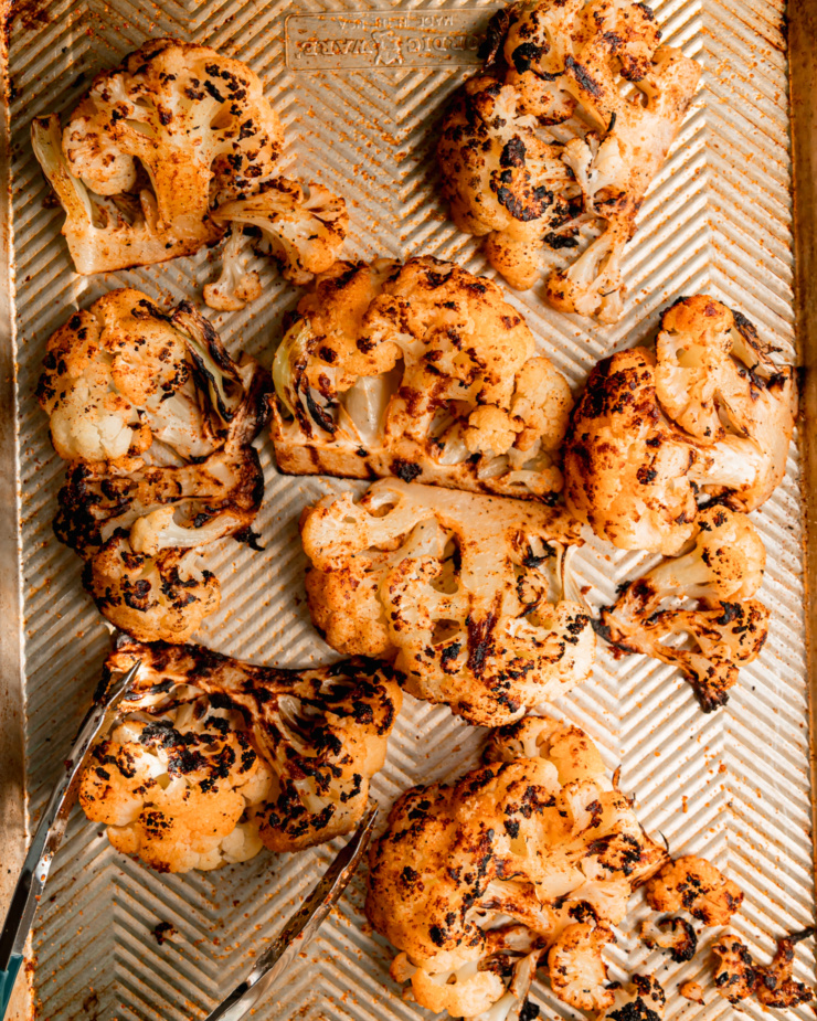 An overhead shot shows grilled cauliflower wedges and a set of tongs on a baking sheet.