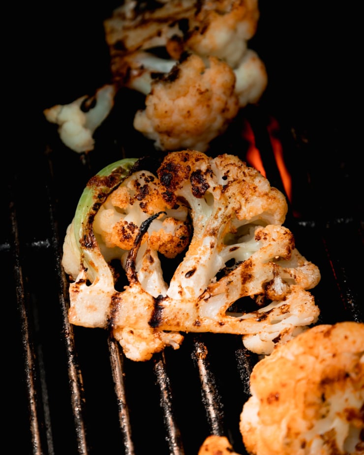 A 3/4 angle shot shows cauliflower with char marks on BBQ grill grates.