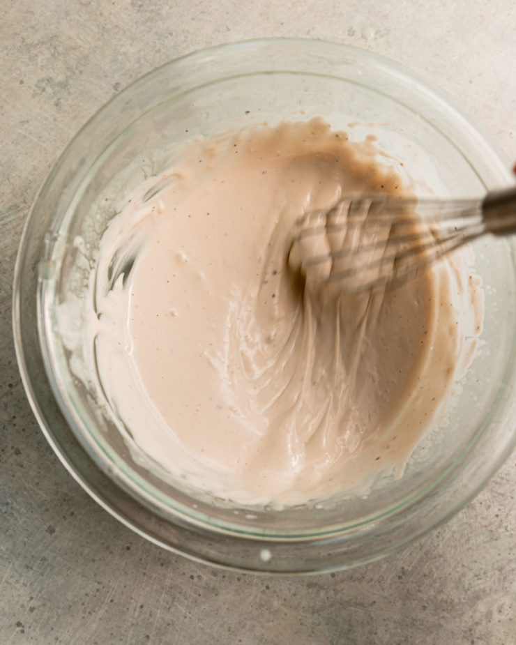 An overhead shot shows a yogurt tahini sauce being whisked up in a small glass bowl.