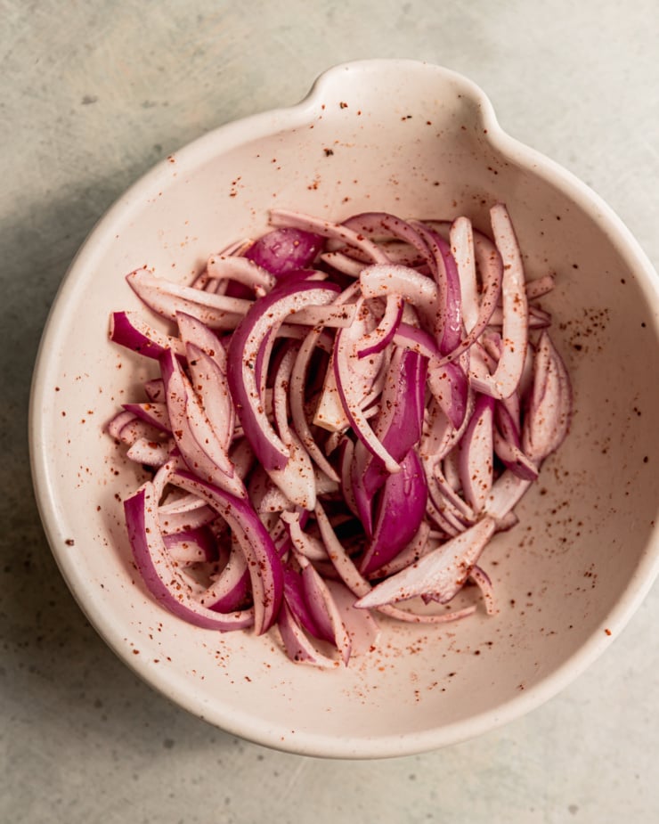 An overhead shot of sumac-pickled red onions in a small, beige bowl.