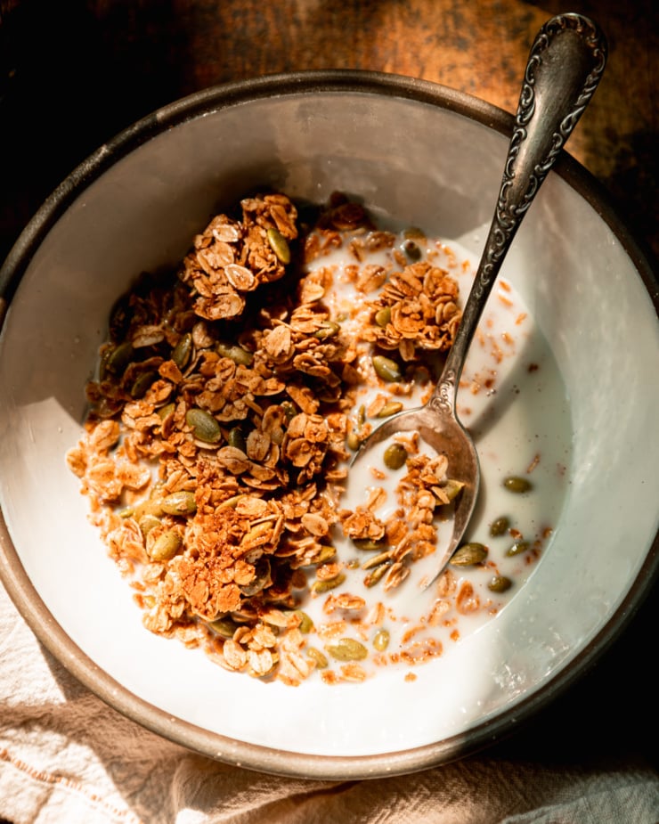 An overhead shot shows a ceramic bowl with pumpkin seed granola and some almond milk in bright sunlight.
