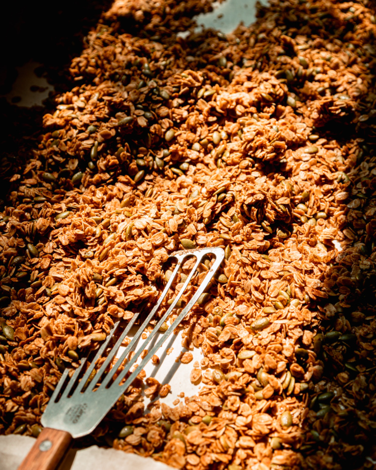 A 3/4 angle image shows a baking sheet of pumpkin seed granola with a metal spatula sticking out.
