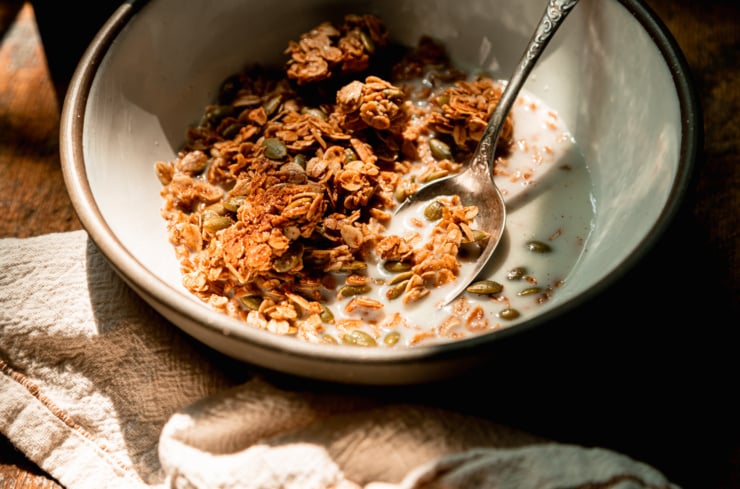 A 3/4 angle image shows a bowl with granola and almond milk in direct sunlight.