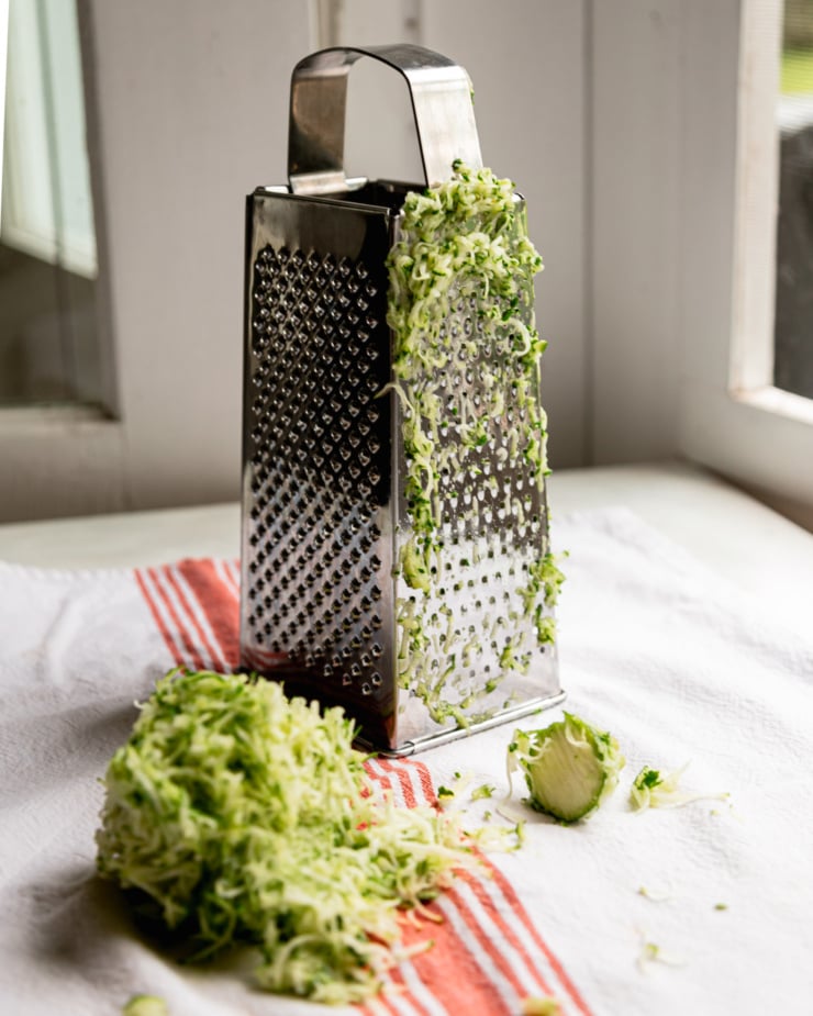 A head-on shot shows a box grater and a pile of shredded zucchini nearby.