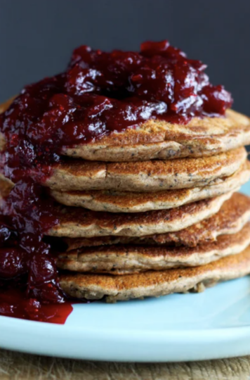 A head on shot shows a stack of vegan dirty masala chai pancakes on a blue plate. The pancakes are topped with a cranberry compote.
