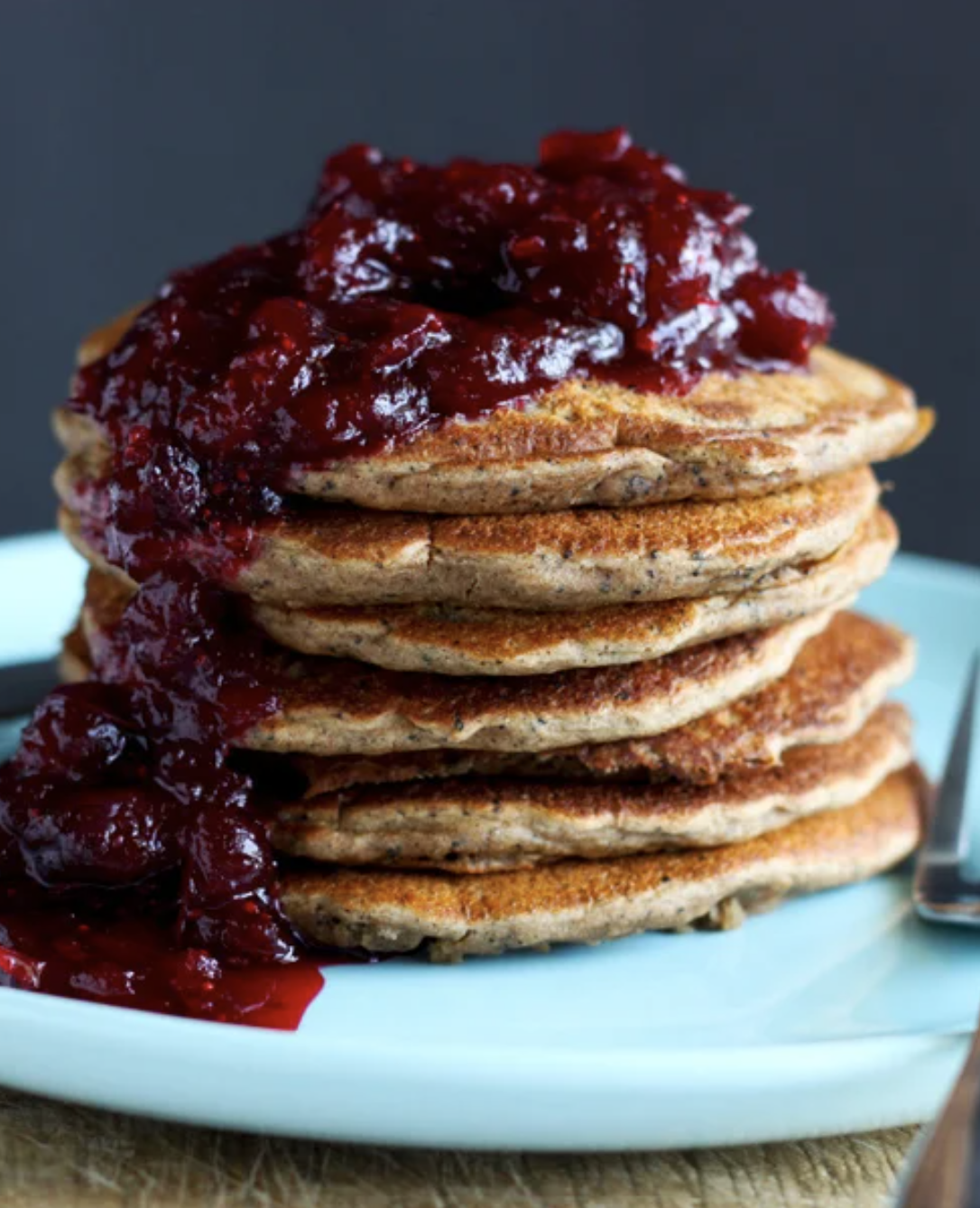 A head on shot shows a stack of vegan dirty masala chai pancakes on a blue plate. The pancakes are topped with a cranberry compote.