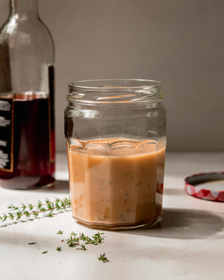 A head-on shot of a jar of red wine vinegar dressing with thyme leaves scattered around.