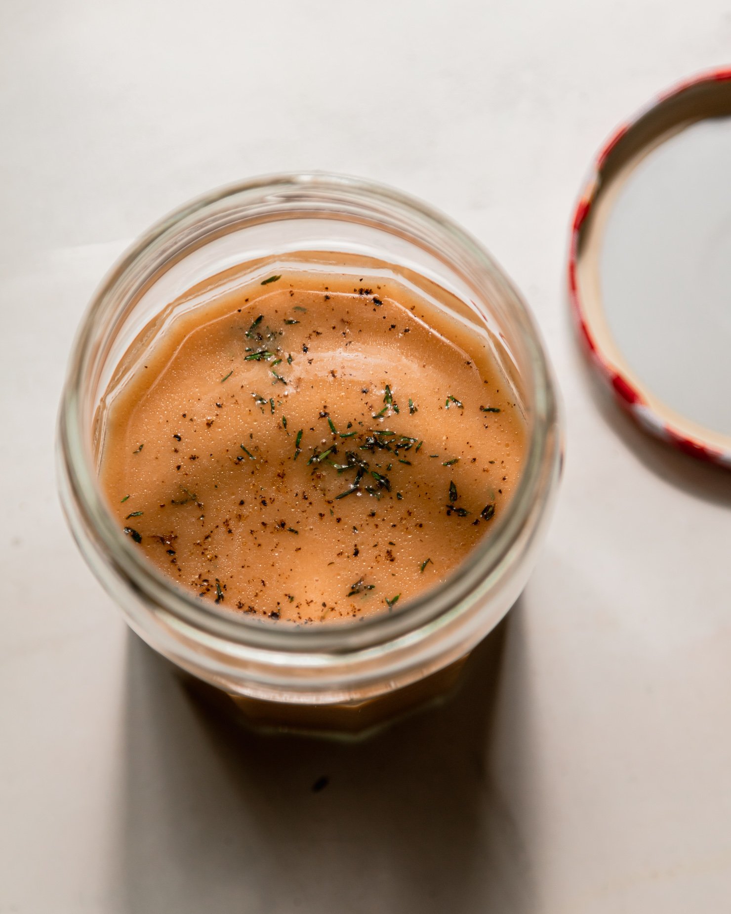 An overhead shot of a jar of red wine vinegar dressing with fresh thyme.