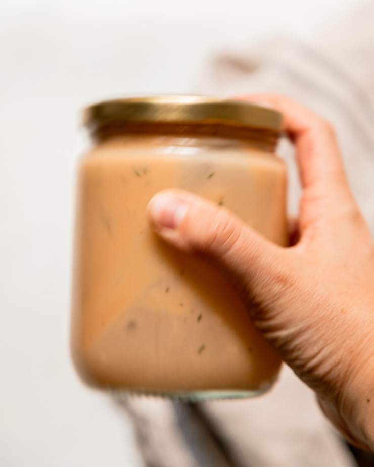 An overhead and blurry shot shows a hand shaking up a jar of salad dressing.