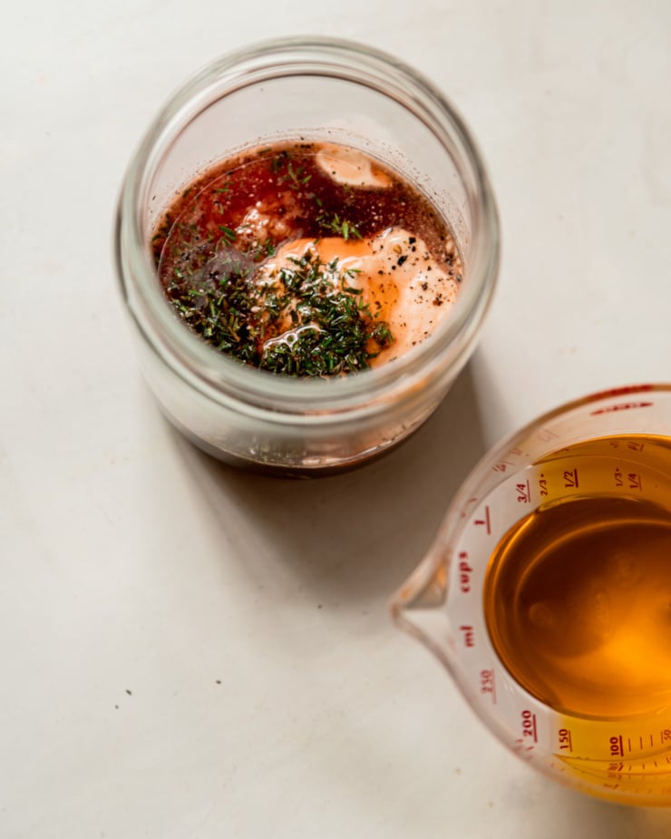 An overhead shot shows a salad dressing being made in a glass jar. A measuring cup of olive oil is nearby.