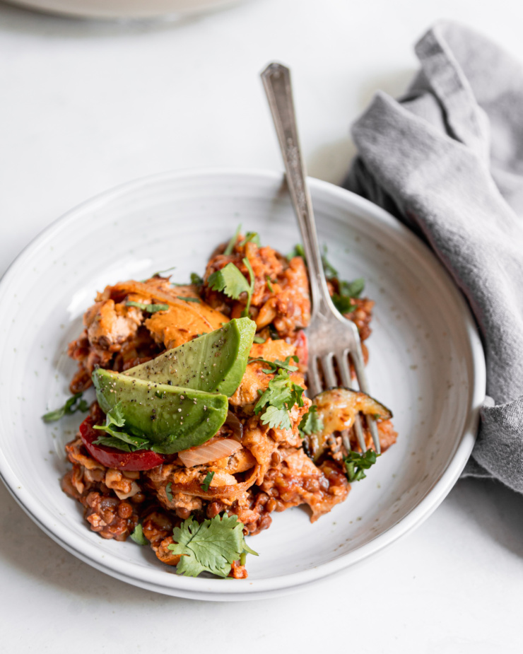 A single serving of chopped vegan enchilada skillet. The serving is in a wide ceramic bowl and topped with avocado slices and chopped cilantro.