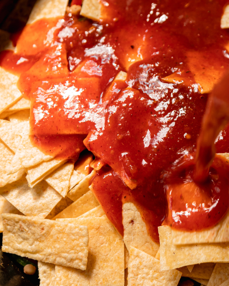 An up close shot shows chopped tortillas being tossed in a red sauce mixture.