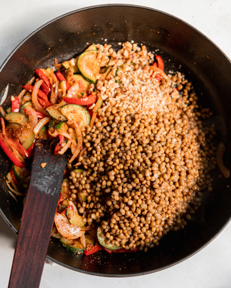 An overhead shit shows finely chopped walnuts and cooked lentils that have been newly added to a skillet with sautรฉed vegetables.