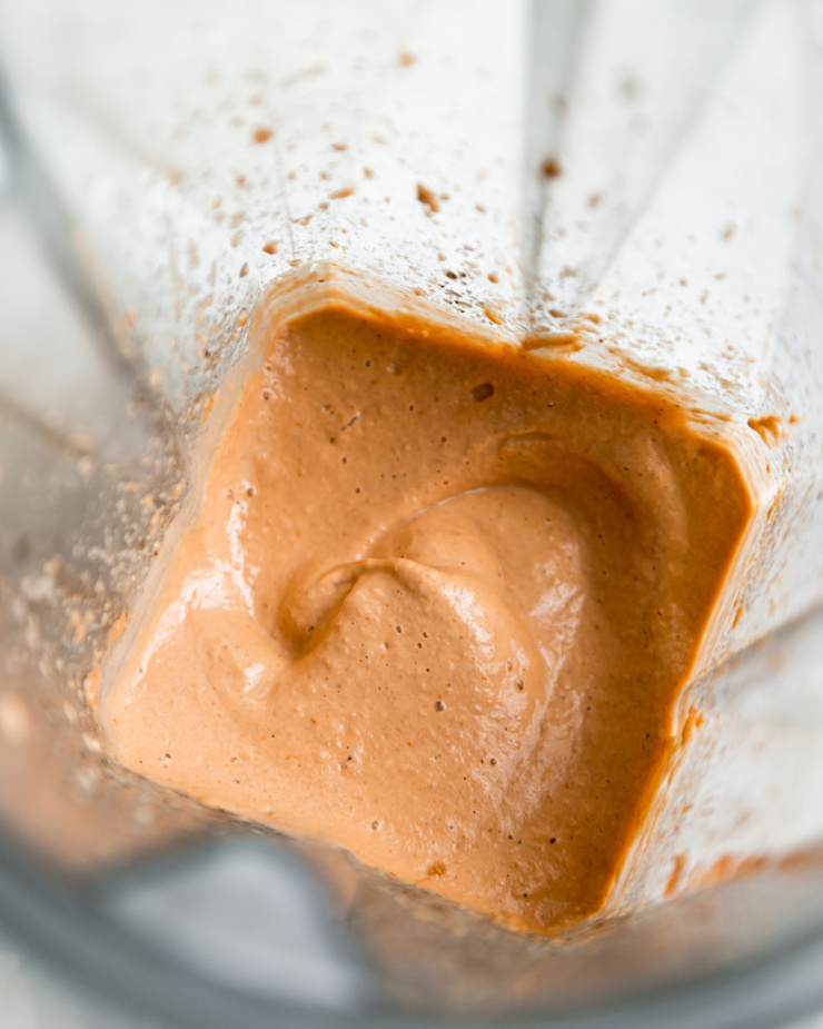 An up close, overhead shot shows a sunflower seed-based "cheese" topping that has been just mixed up in a blender container.