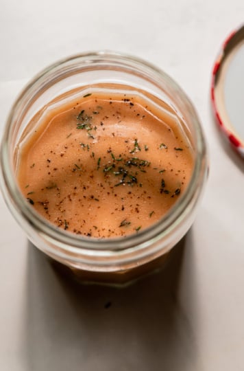 An overhead shot of a jar of red wine vinegar dressing with fresh thyme.