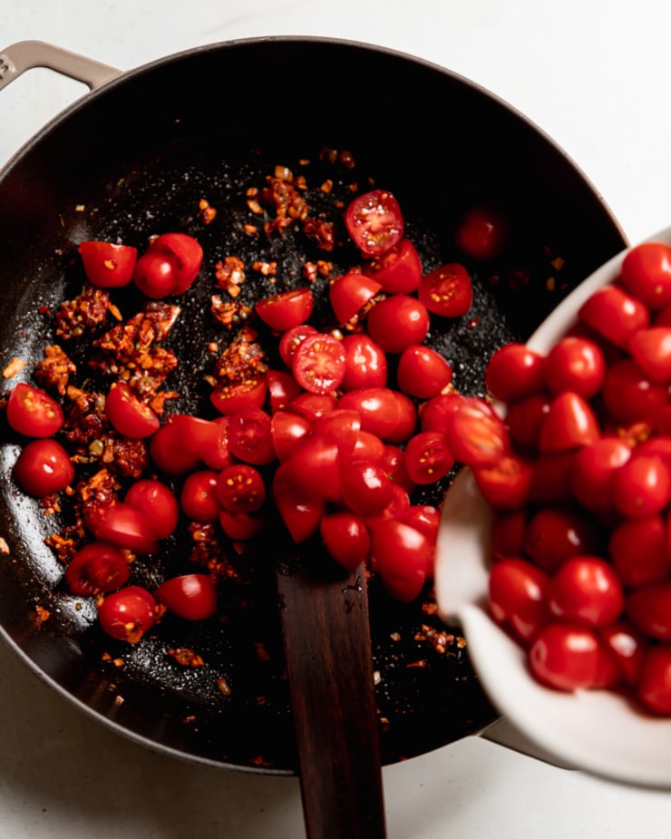 An overhead shot shows halved cherry tomatoes being poured into a pot.
